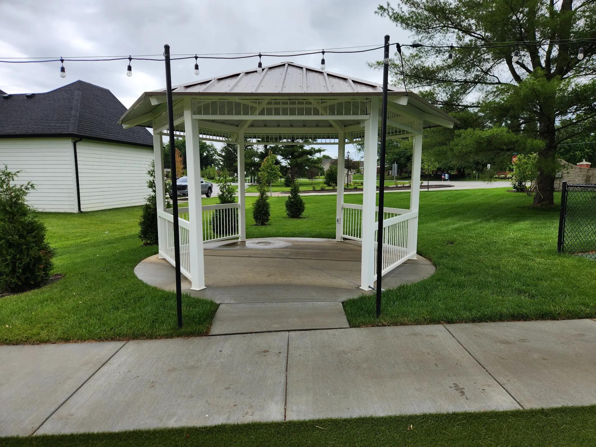 Octagonal powder coated steel gazebo with decorative railings and metal roof in residential park setting